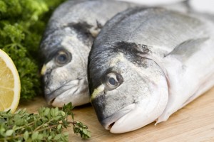 Two fresh sea bream on wooden board with herbs and lemon